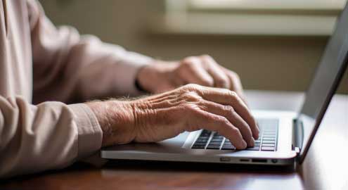 Older person typing on a laptop.