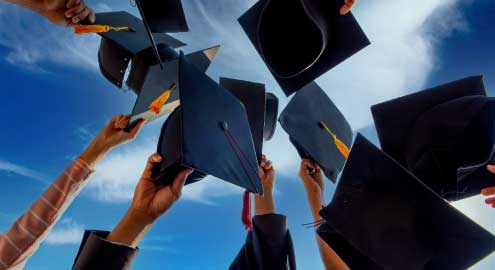 Graduates in their cap and gown tossing their cap in the air.