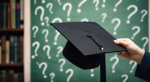 Person holding a graduation cap with multiple question marks in the background.