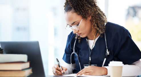 Medical student writing in their planner in front of a laptop.